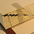 Spine cross-section showing French or link sewing over linen tapes and spine linings. The staggered printed bars on the folds indicate the sequence of the signatures.